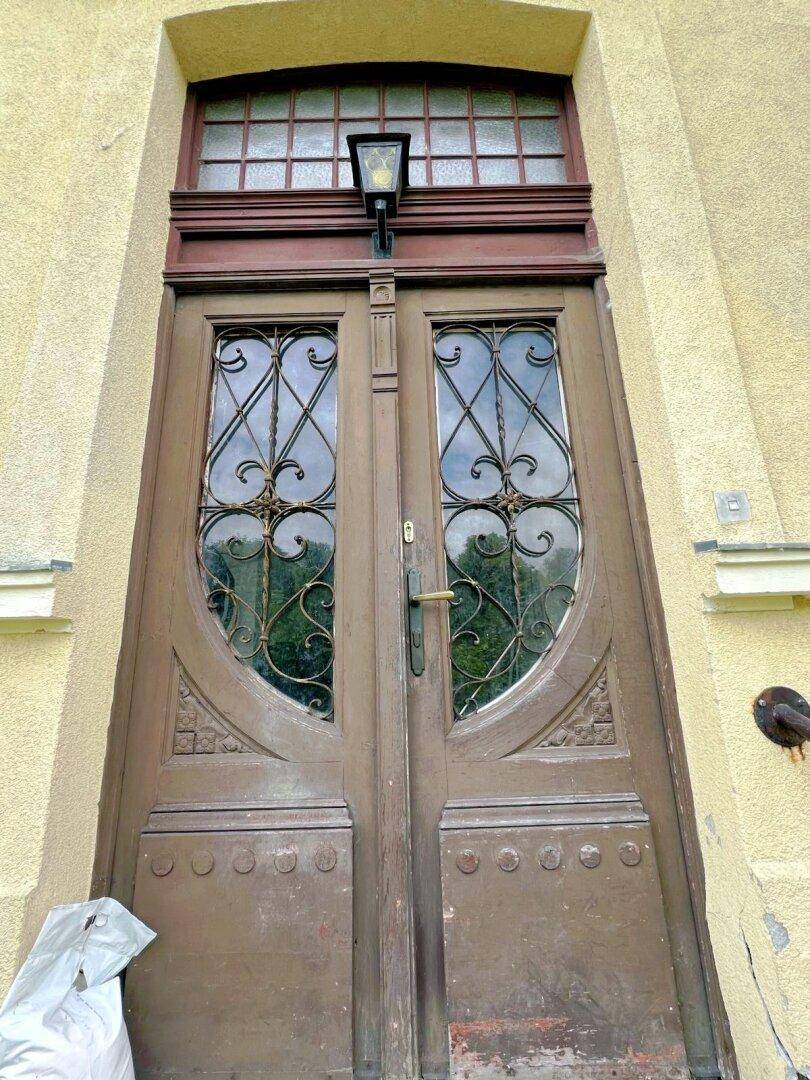 Historische Holztür mit kunstvollen Glas- und Metallverzierungen, die zum Innenbereich führt.