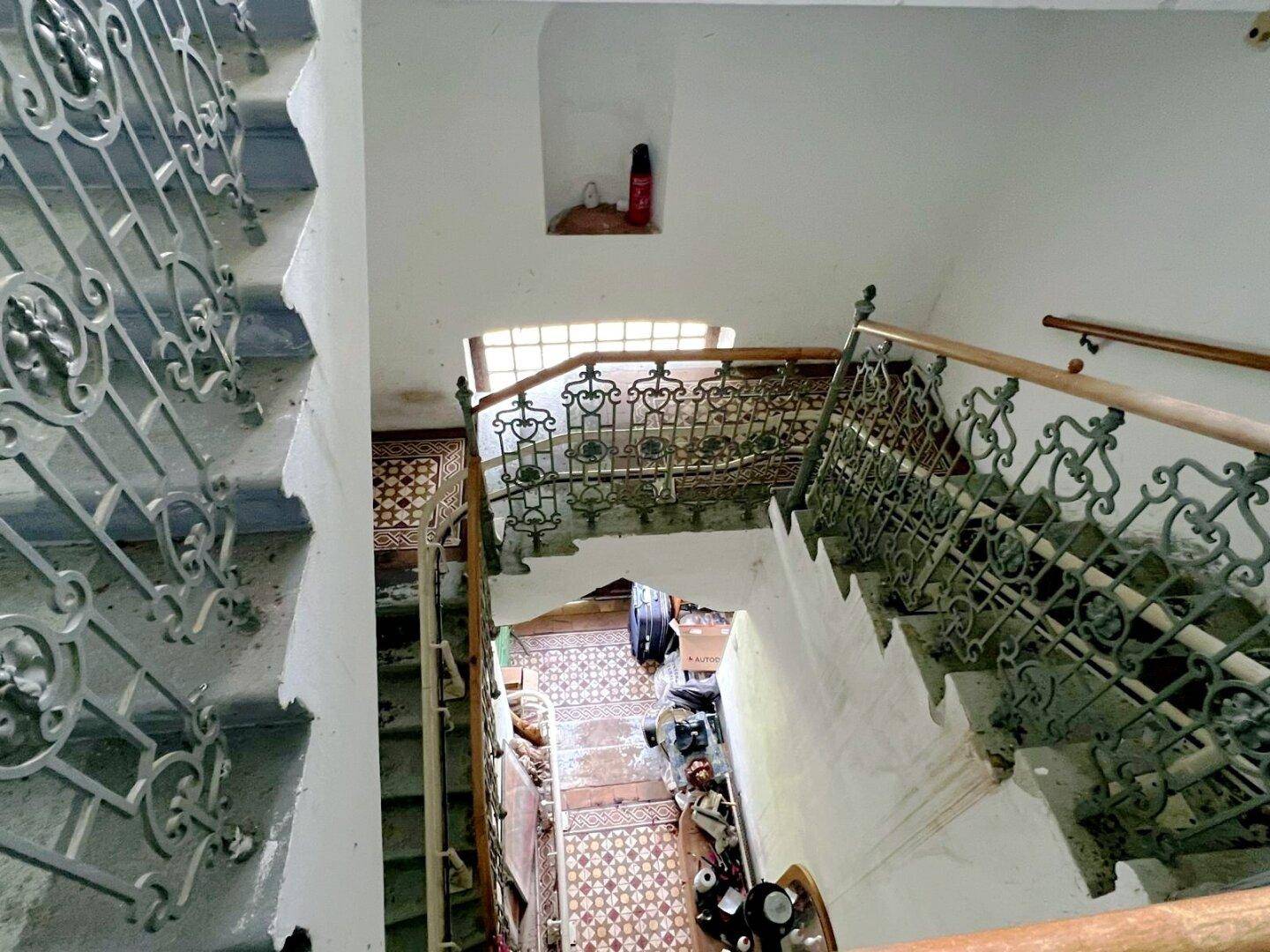 Historisches Treppenhaus mit schmiedeeisernem Geländer und gemusterten Fliesenböden.
