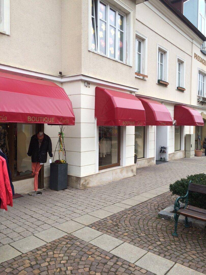 Außenansicht einer Boutique mit roten Markisen über den Schaufenstern und einem gepflasterten Gehweg.