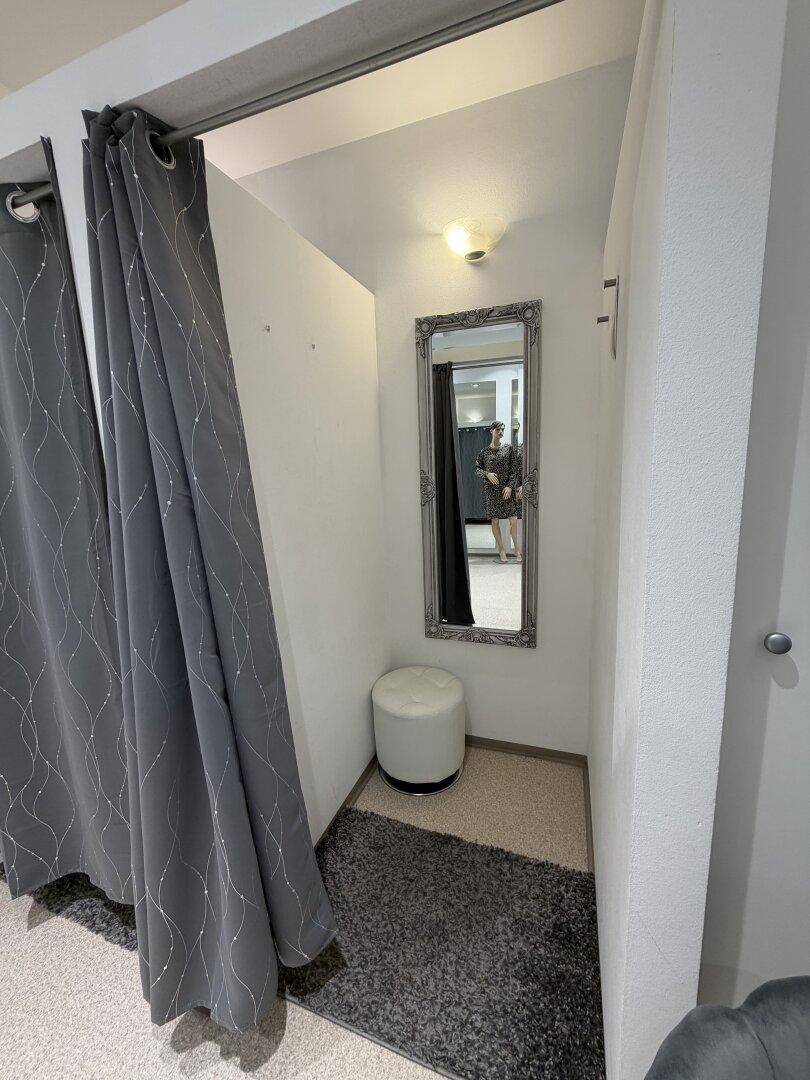 Innenansicht einer Ankleidekabine mit Spiegel, Hocker und Teppichboden für Komfort.