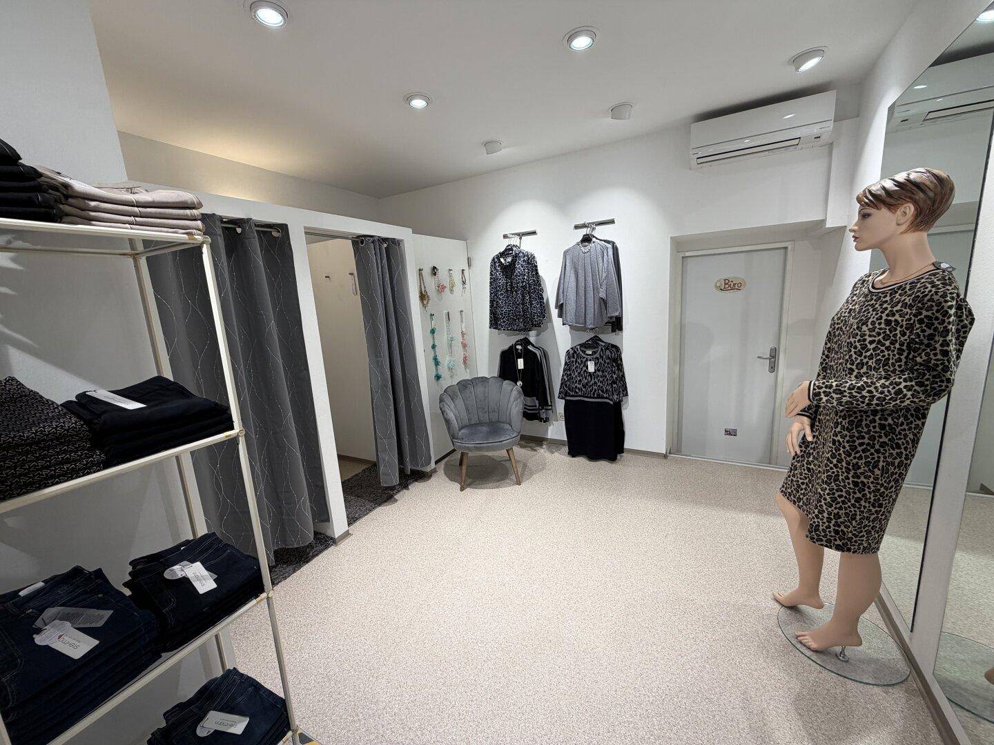 Ankleidebereich einer Boutique mit Vorhängen, einem Sessel und einer Klimaanlage an der Wand.