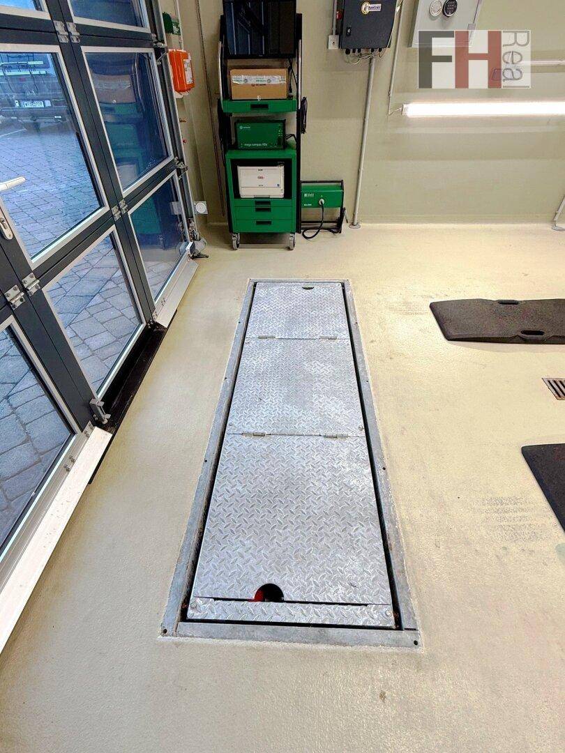 Innenansicht einer modernen Werkstatt mit eingelassener Prüfplattform, Diagnosestation und großer Glas-Garagentür für natürliches Licht.