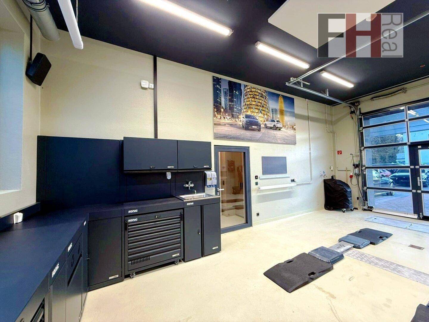 Moderne Werkstatt mit schwarzen Einbauschränken, Spülbecken, großer Wandgrafik und einer breiten Glas-Garagentür.