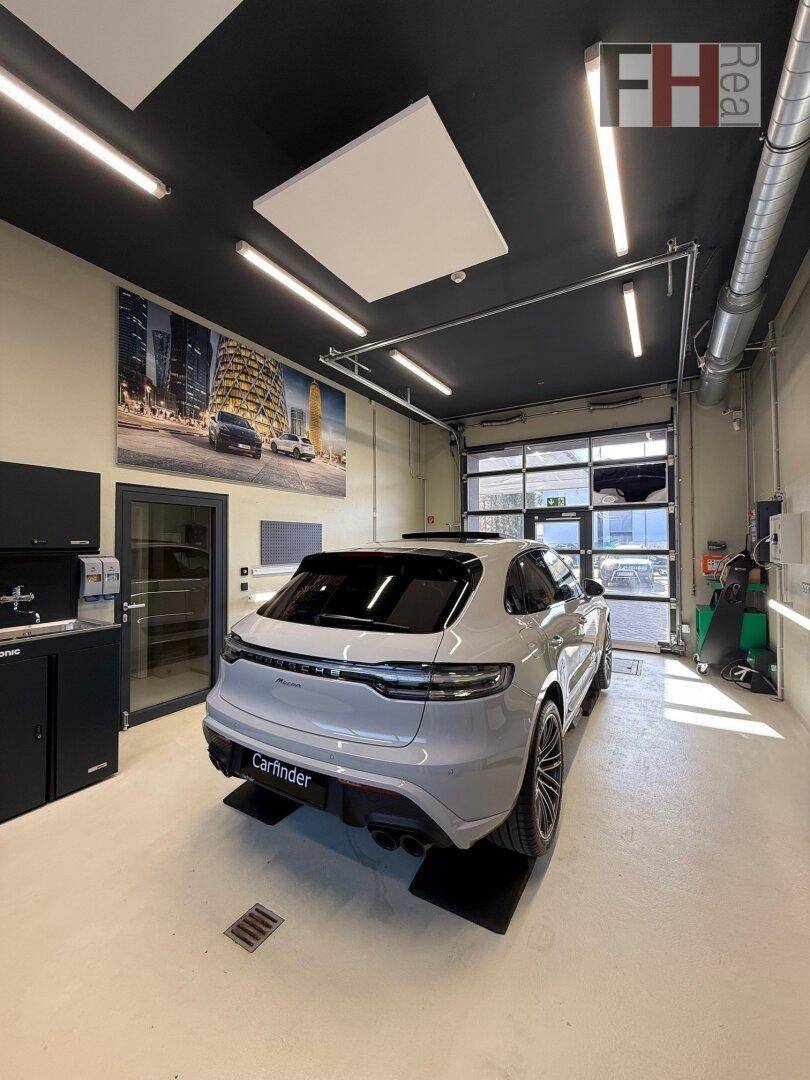 Ein grauer Porsche SUV steht in der modernen Werkstatt, mit Blick auf die große Glas-Garagentür und die Deckenbeleuchtung.