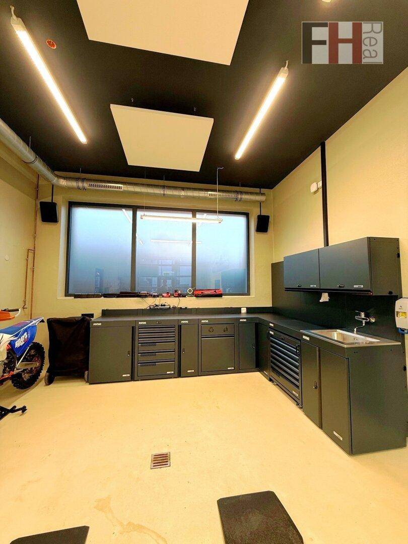 Ansicht der schwarzen Einbauschränke und Arbeitsflächen in der Werkstatt, mit einem Motorrad und einem großen Fenster.