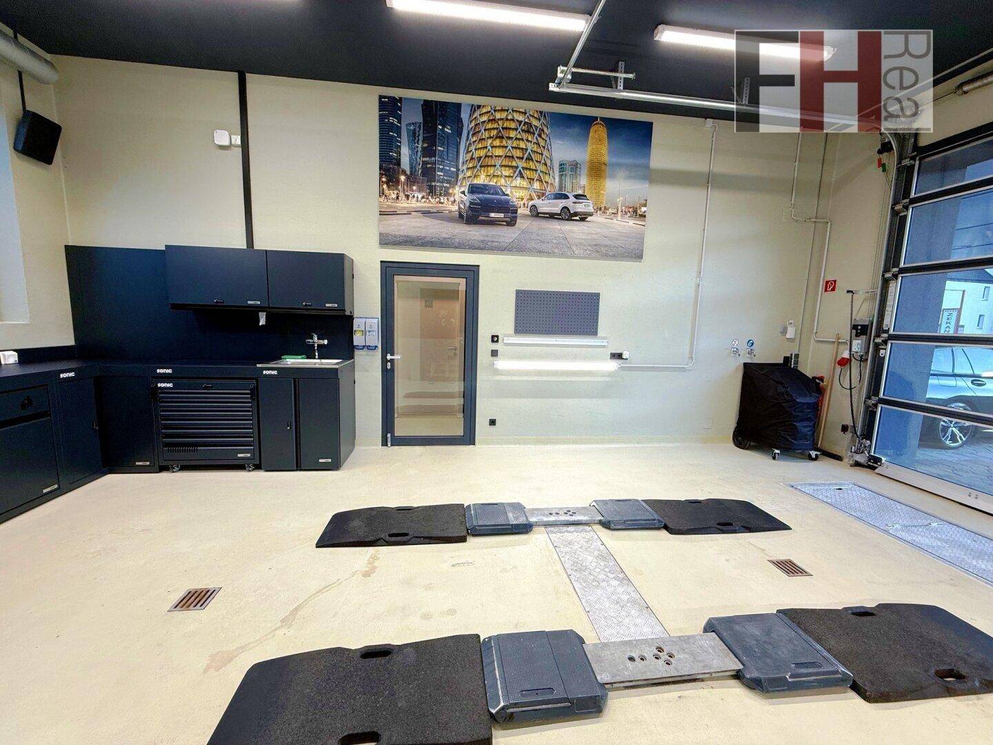 Geräumige Werkstatt mit schwarzen Einbauschränken, Wandgrafik und Fahrzeugprüfgeräten auf dem Boden.