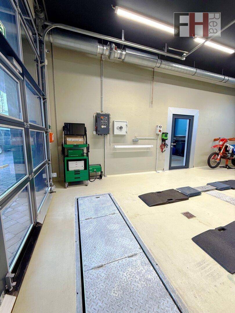 Blick auf die Glas-Garagentür und die eingelassene Fahrzeugprüfplattform in der Werkstatt, mit Diagnosestation und Motorrad.