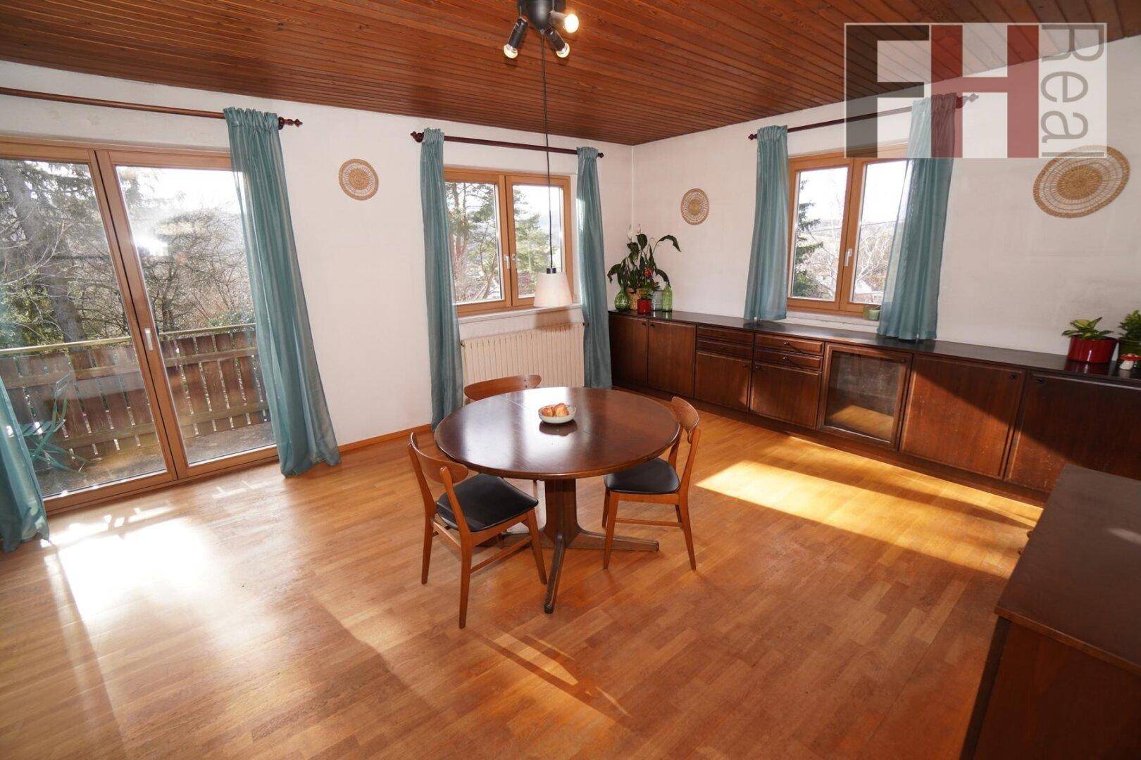 Heller Essbereich mit Holzboden, Holzdecke und Zugang zu einem sonnigen Balkon.