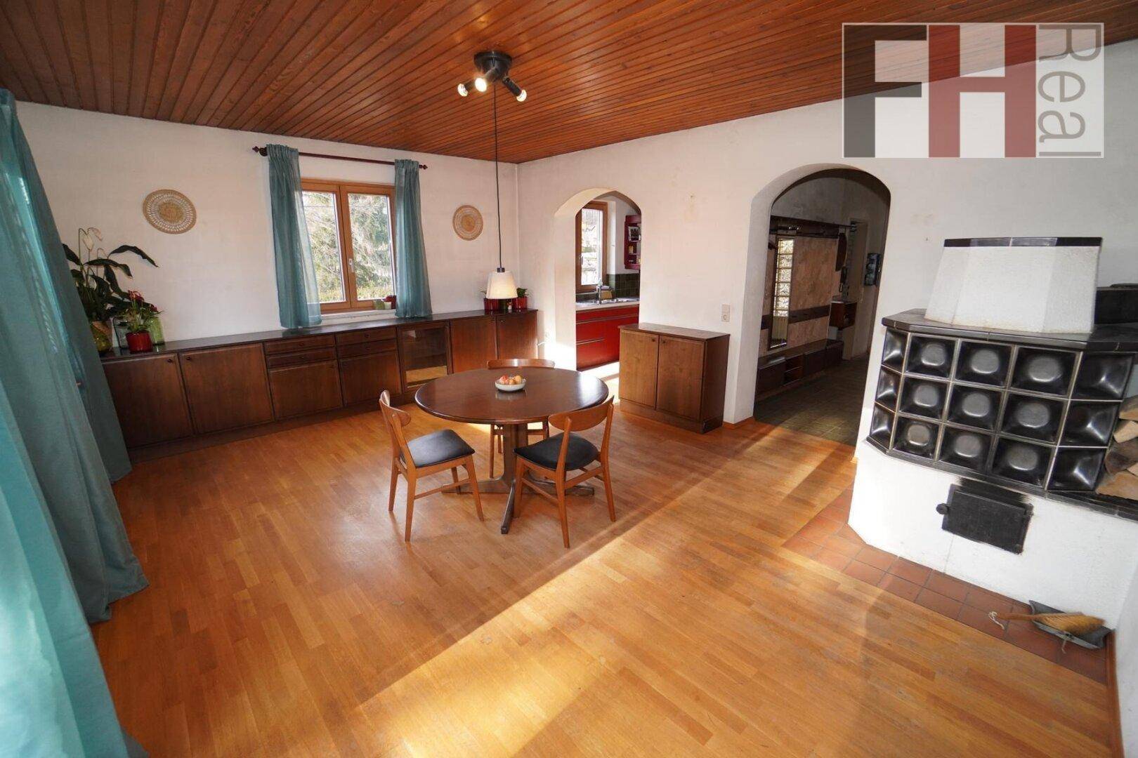 Geräumiger Wohn-Essbereich mit traditionellem Kachelofen, Holzboden und viel Tageslicht.