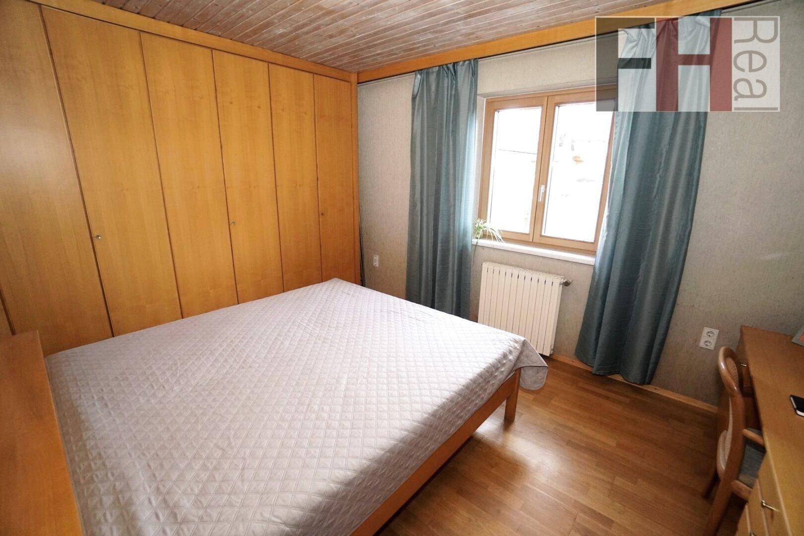 Schlafzimmer mit Holzboden, Einbauschränken und Fenster mit Vorhängen.