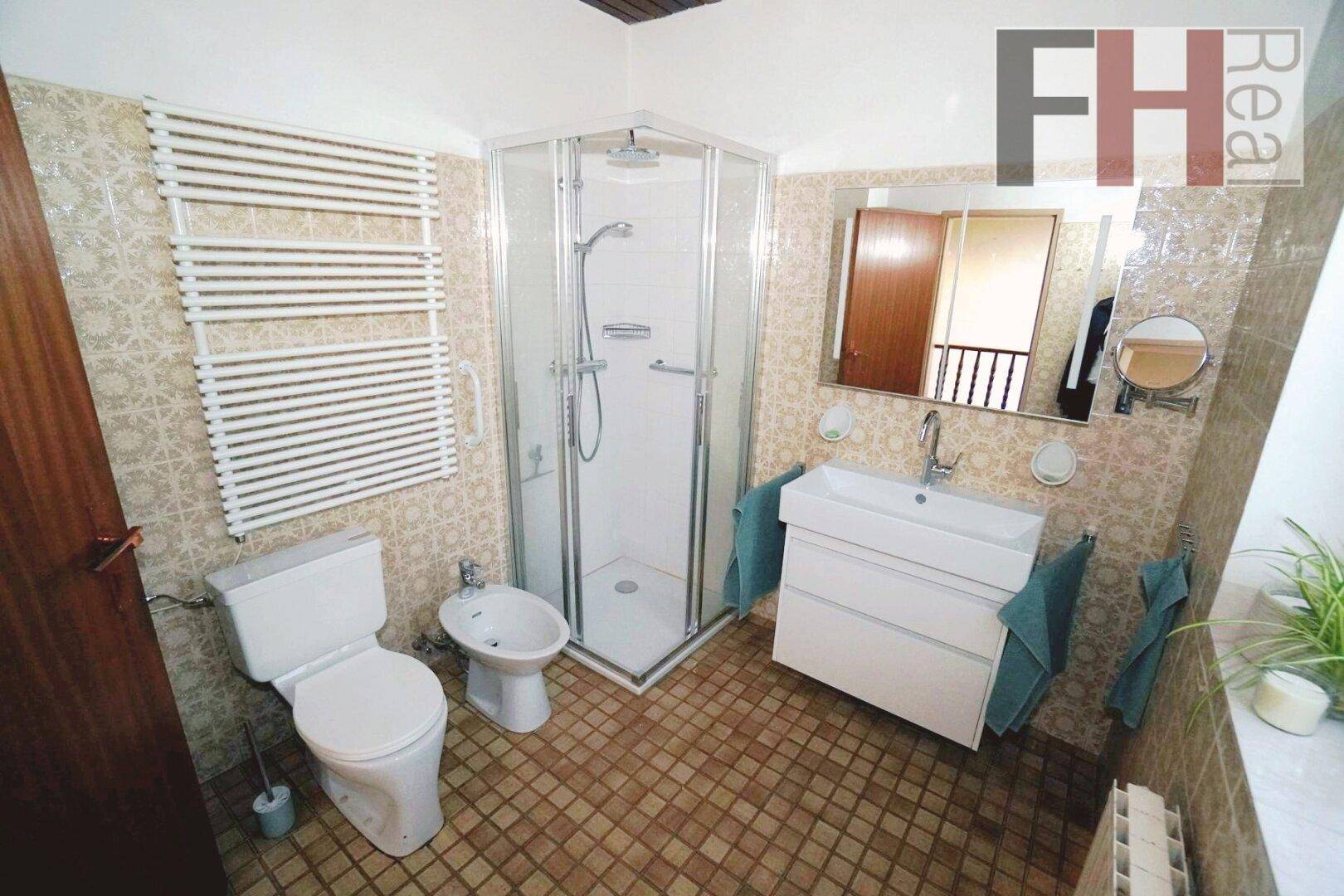 Badezimmer mit Dusche, WC, Bidet und beheiztem Handtuchhalter in beigen Fliesen.