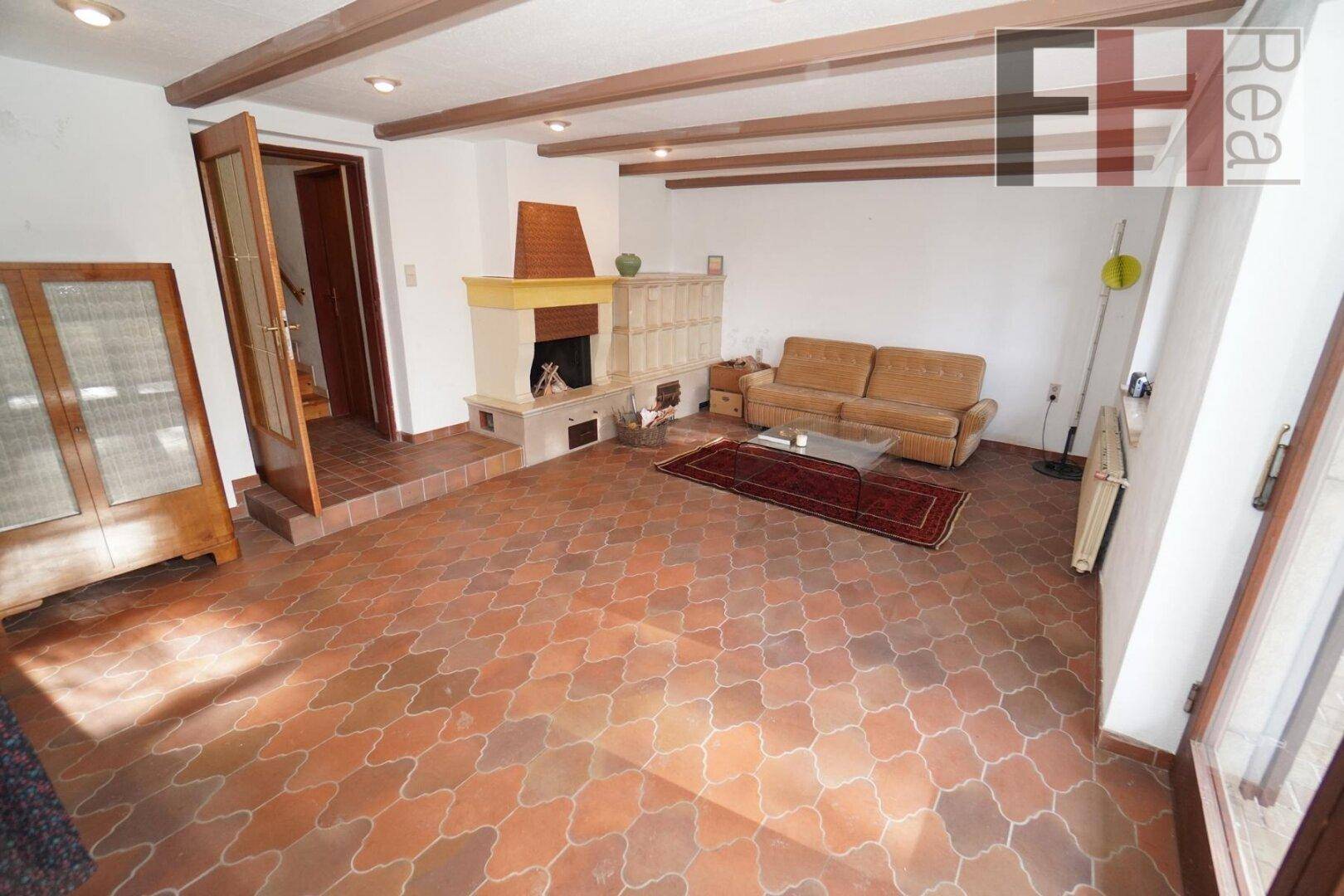 Geräumiges Wohnzimmer mit Kamin, Holzbalken und Terrakotta-Fliesenboden.