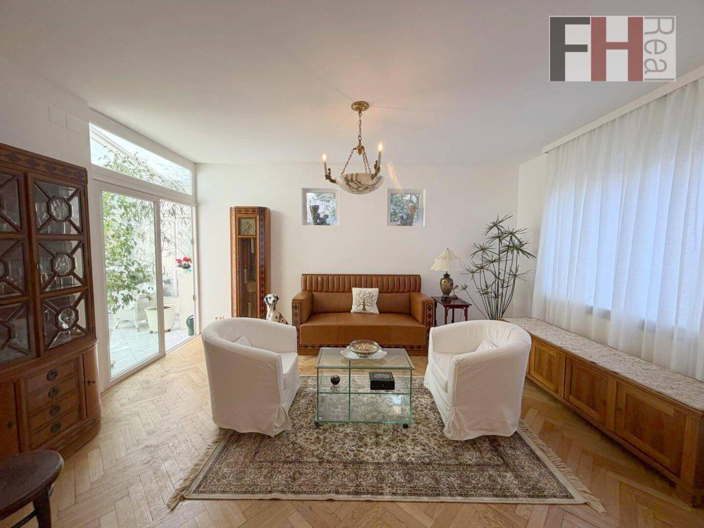 Wohnzimmer mit Parkettboden, großen Fenstern und Zugang zum Wintergarten.