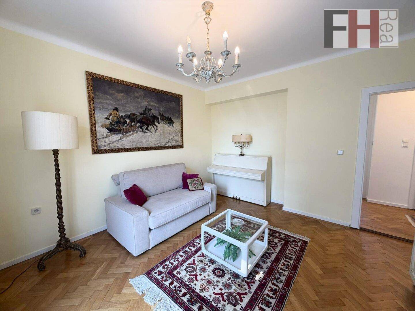 Heller Wohnraum mit Parkettboden, Sofa und dekorativem Kronleuchter.