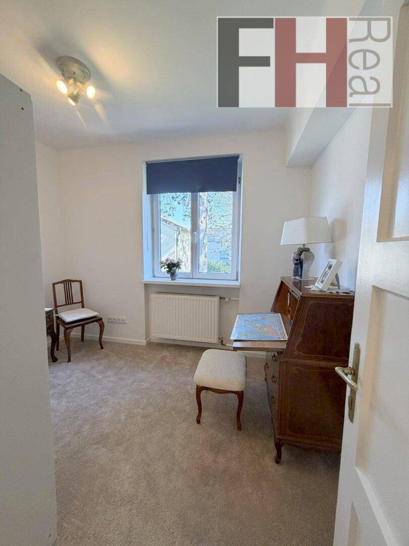 Kleines Arbeitszimmer mit Teppichboden, Schreibtisch und Fenster.