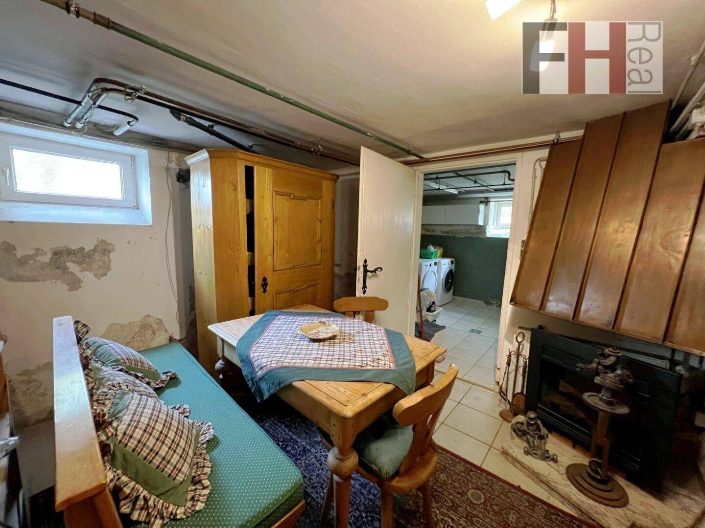 Rustikaler Kellerraum mit Kamin, Holztisch und Waschküchenzugang.