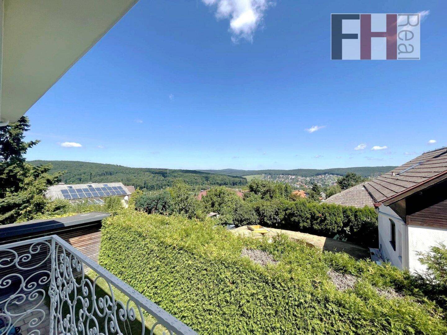 Weitläufiger Ausblick von einem Balkon über die grüne Landschaft und die umliegenden Häuser.