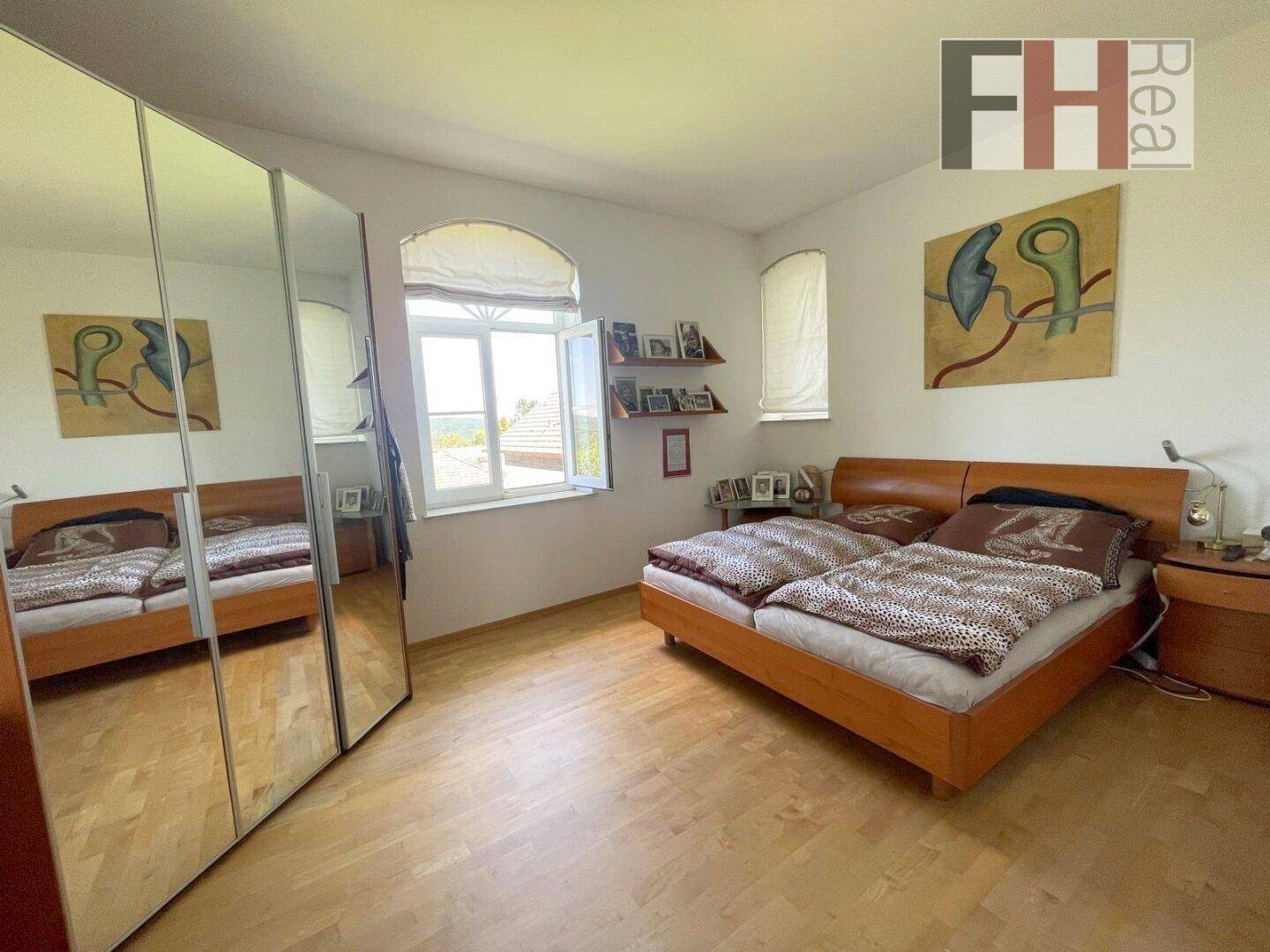 Helles Schlafzimmer mit Parkettboden, großem Spiegelschrank und Blick ins Grüne.