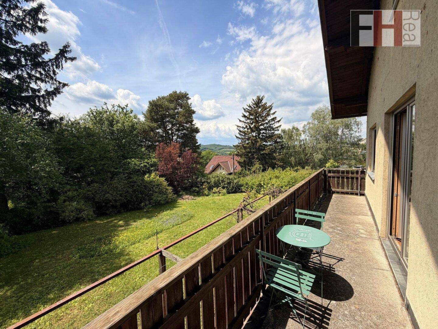 Sonniger Balkon mit Sitzgelegenheiten und weitem Blick über die grüne Landschaft.