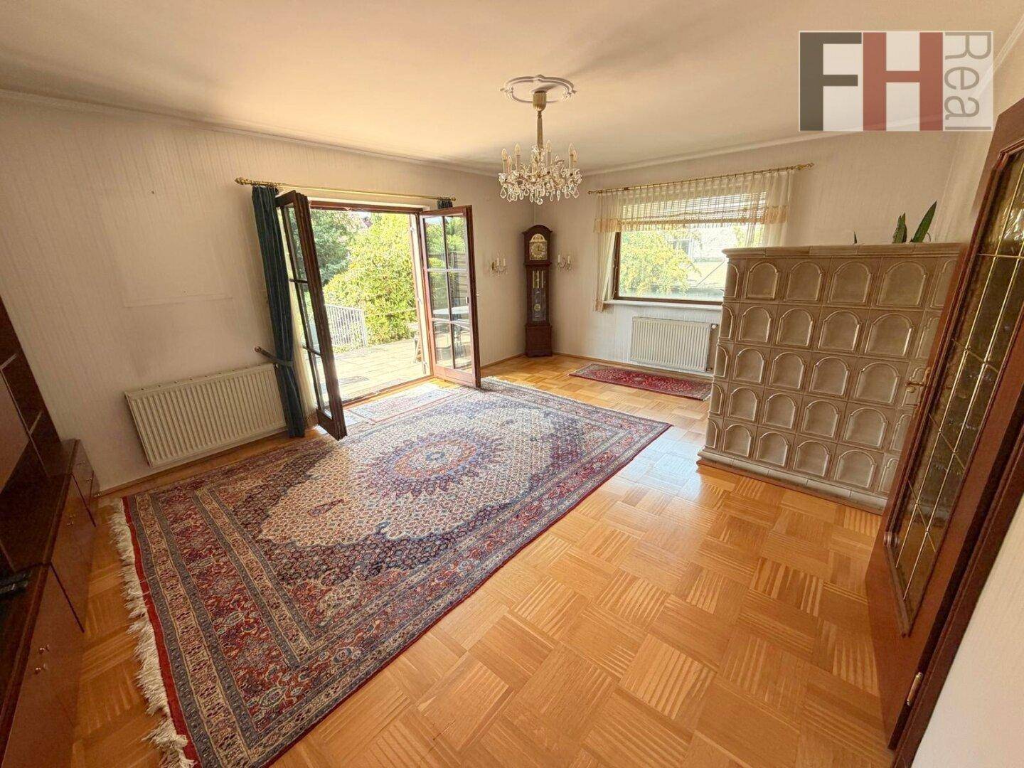 Gemütliches Wohnzimmer mit Fischgrätparkett, großem Teppich und traditionellem Kachelofen.