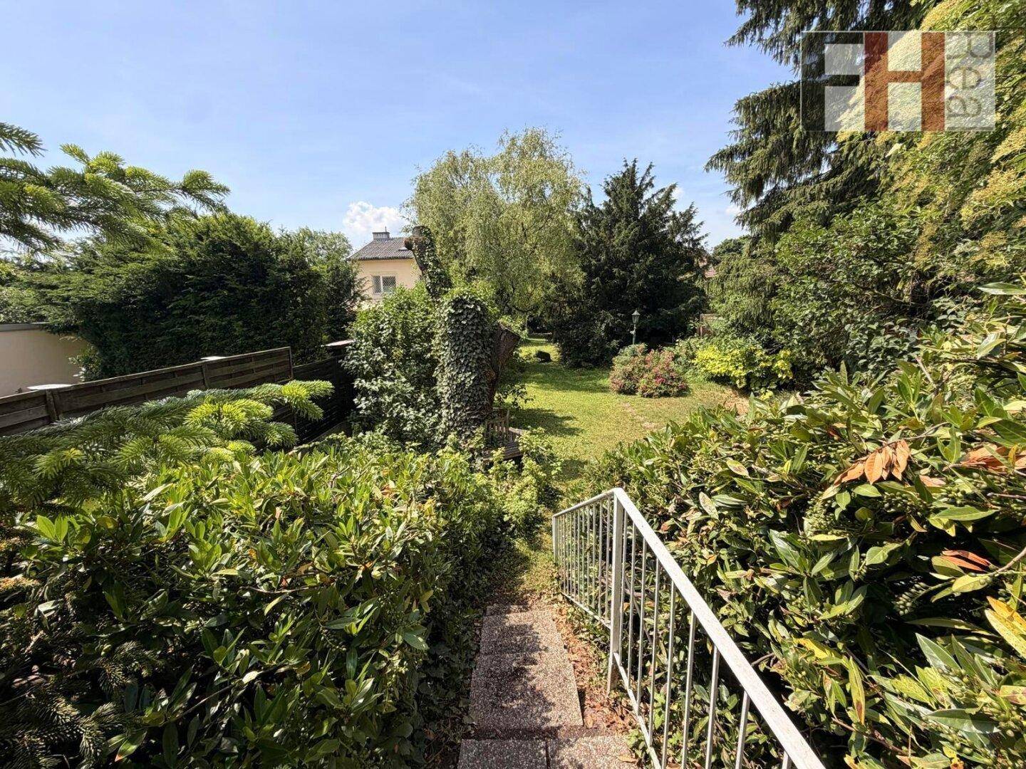 Weitläufiger Garten mit gepflegtem Rasen, hohen Bäumen und einem Steinweg.