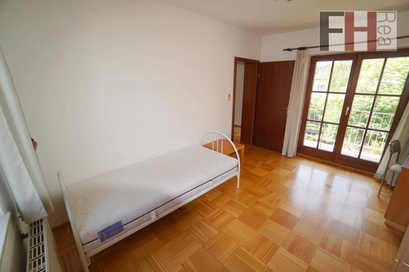 Schlafzimmer mit Parkettboden, Einzelbett und Zugang zu einem sonnigen Balkon.