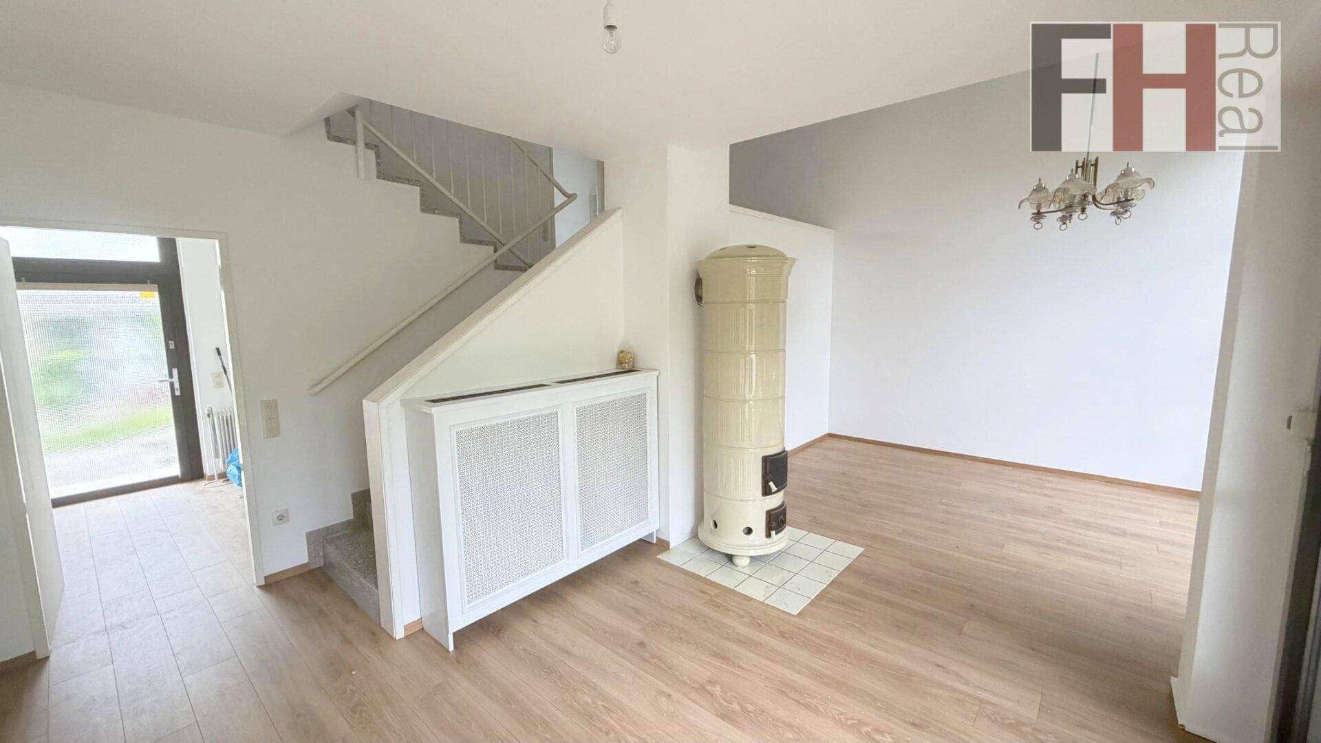 Eingangsbereich mit Treppe, hellem Laminatboden und einem traditionellen Kachelofen im angrenzenden Wohnbereich.