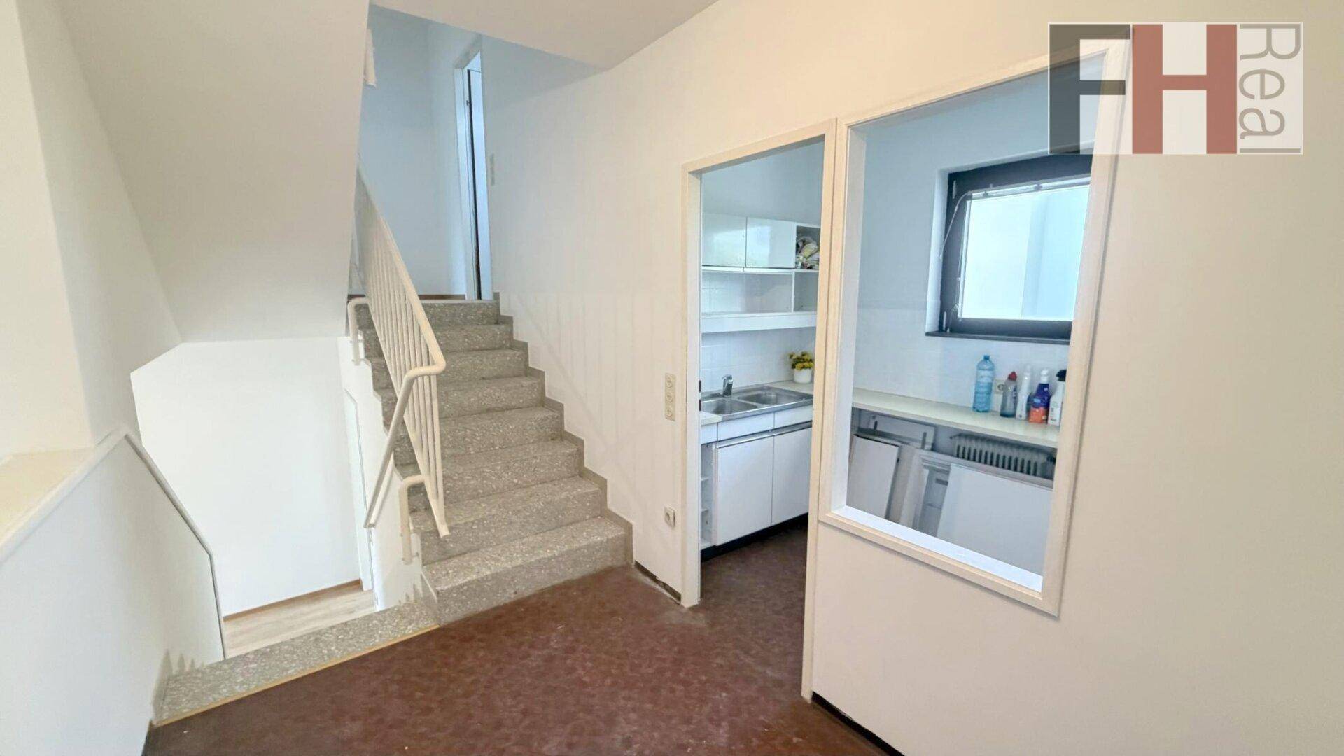 Treppenhaus mit Terrazzostufen und Blick in eine kleine, funktionale Küche mit weißen Schränken.