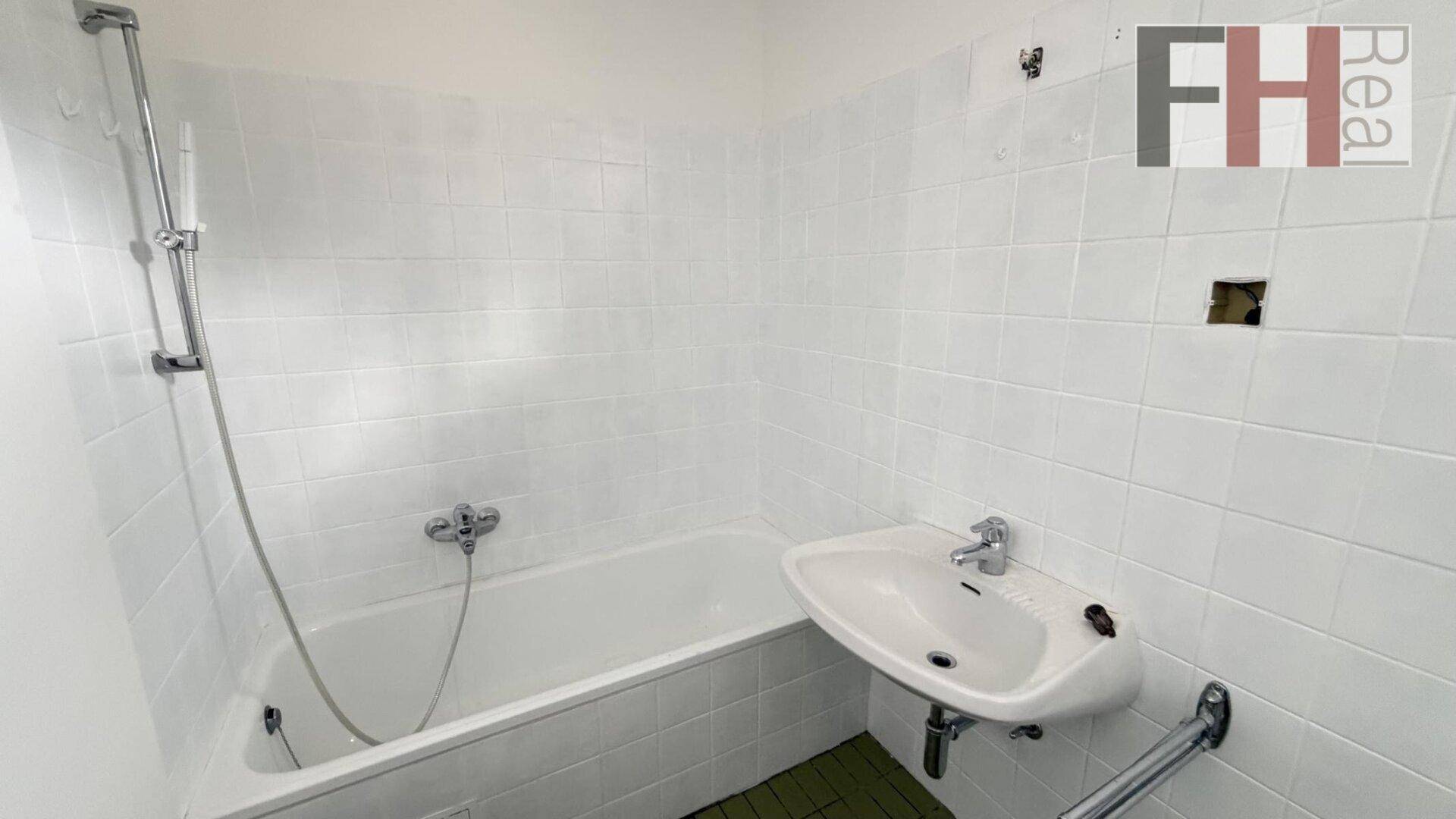 Funktionales Badezimmer mit weißen Fliesen, Badewanne mit Duschfunktion und einem einzelnen Waschbecken.