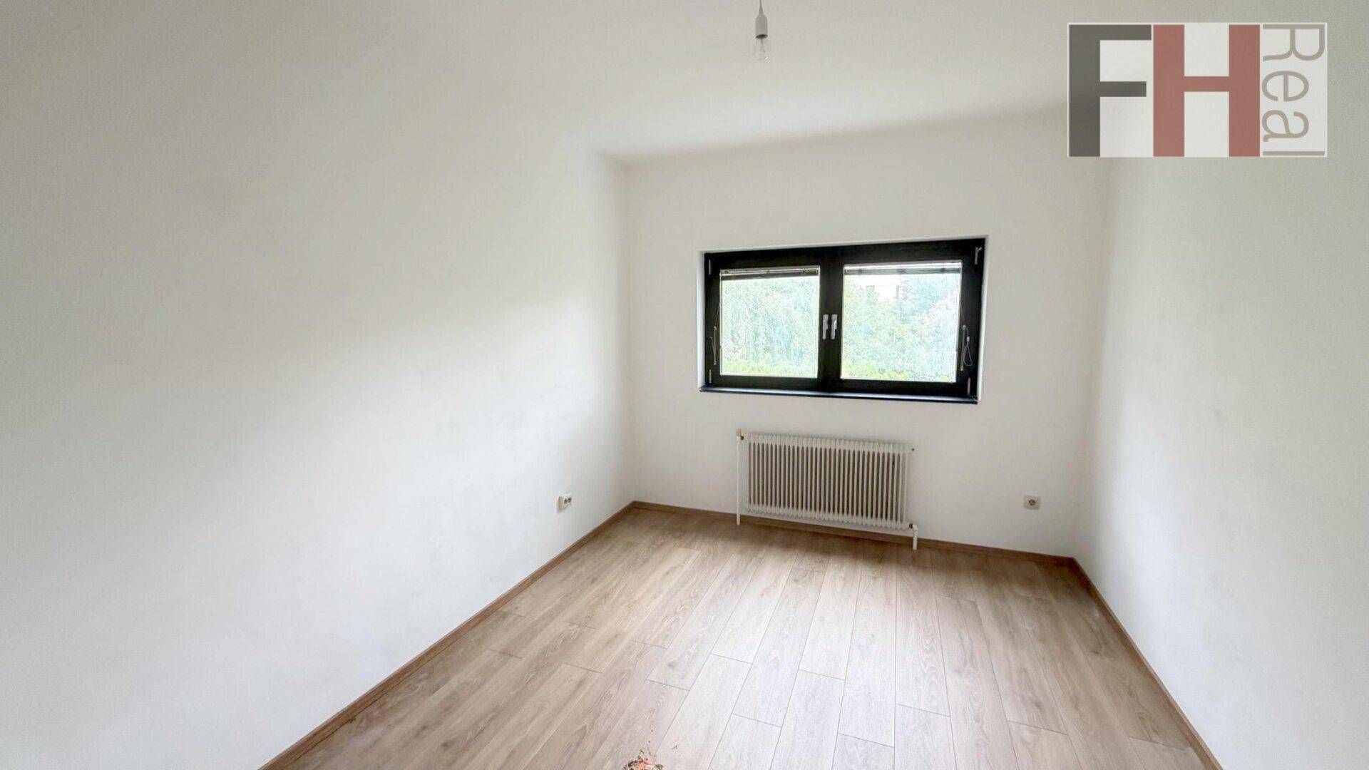 Helles Zimmer mit Laminatboden, weißen Wänden und einem Fenster, ideal als Schlaf- oder Arbeitszimmer.