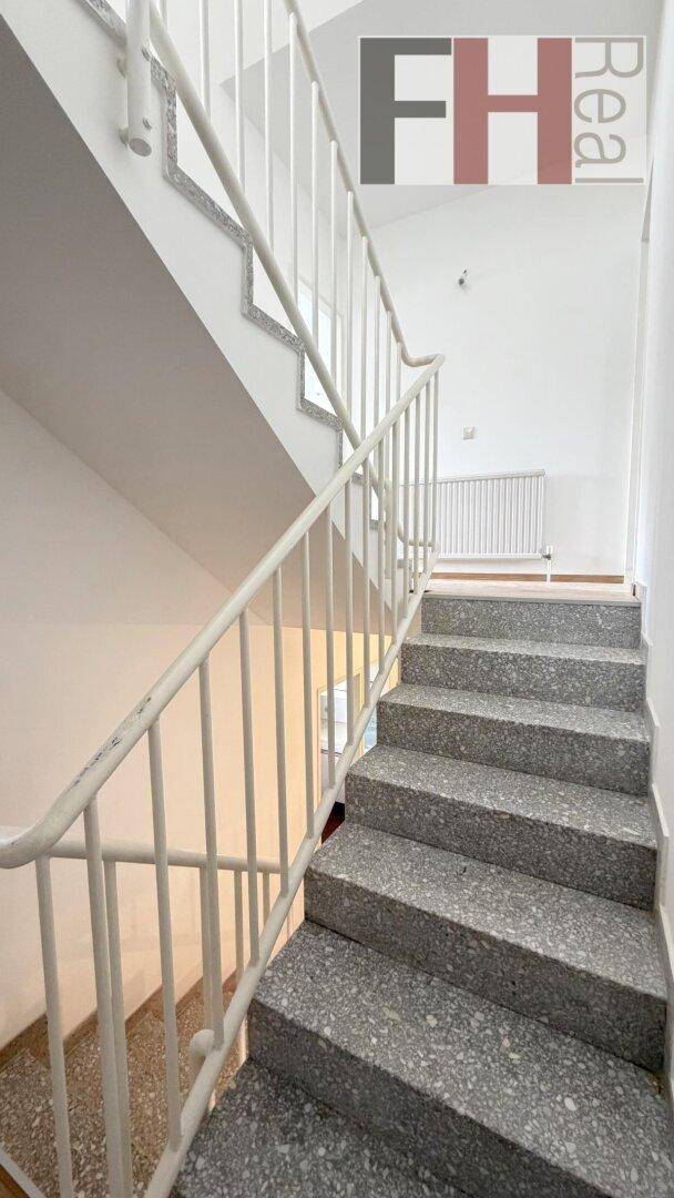 Helles Treppenhaus mit Terrazzostufen und weißem Geländer, das die verschiedenen Etagen verbindet.