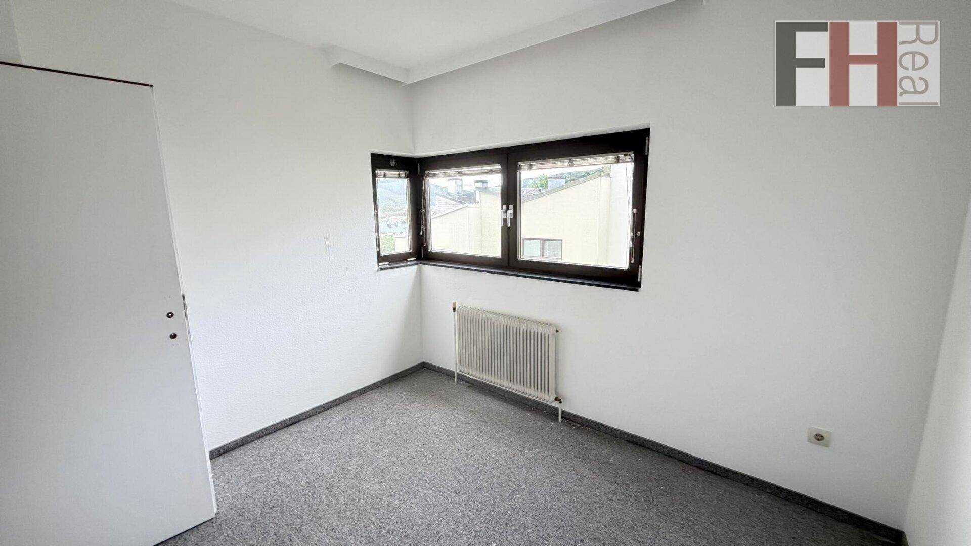Helles Zimmer mit grauem Teppichboden und einem praktischen Eckfenster für viel Tageslicht.