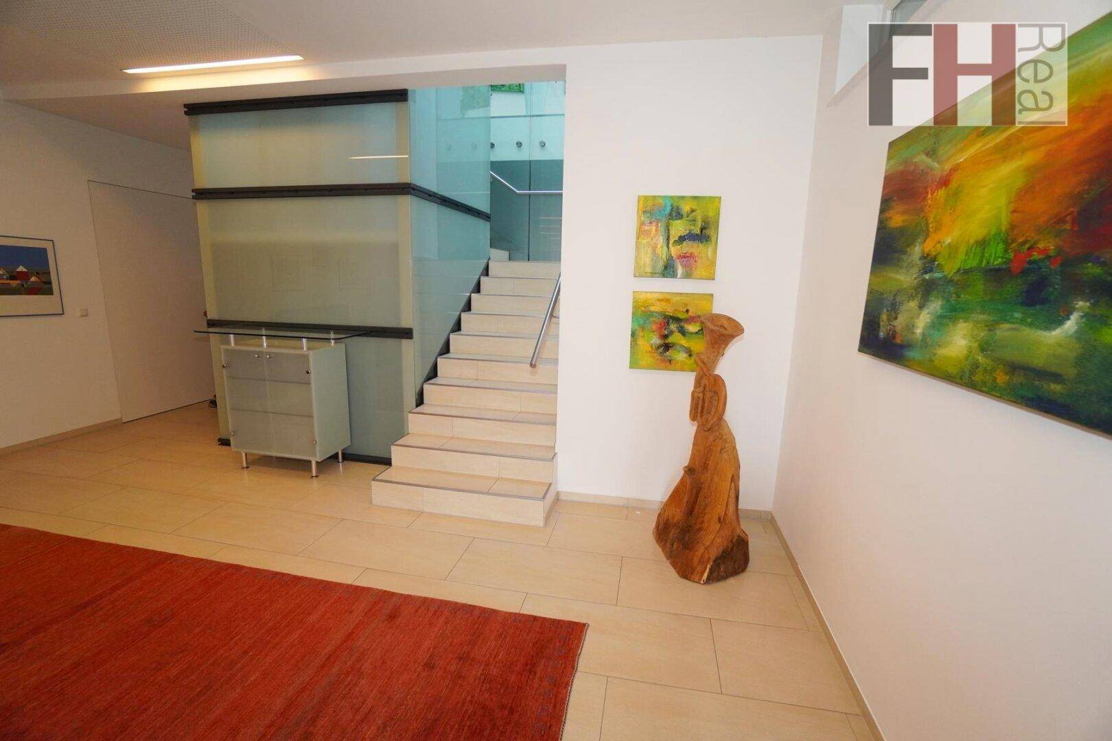 Heller Flur mit Treppenaufgang, modernen Kunstwerken und stilvoller Holzskulptur.