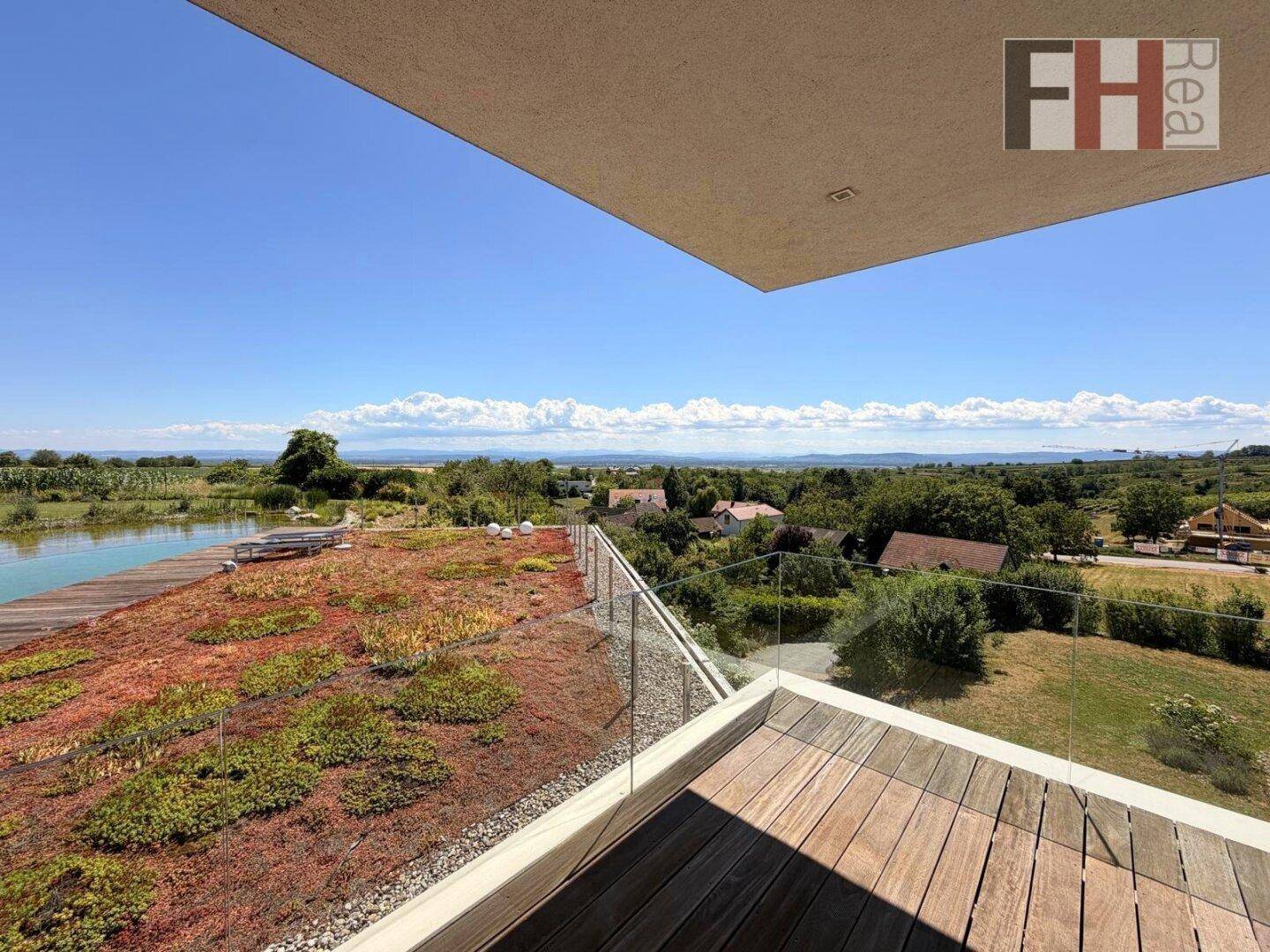 Balkon mit Glasgeländer und weitem Blick über die grüne Landschaft und den Naturpool.
