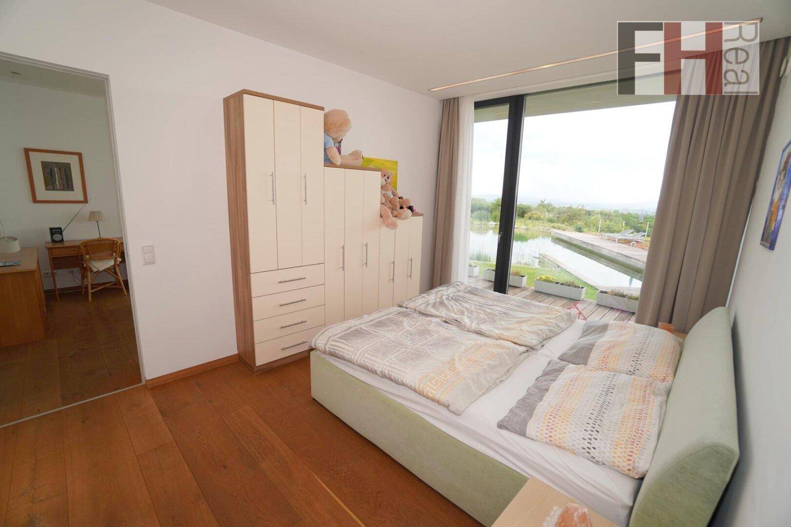 Schlafzimmer mit Holzboden, Einbauschränken und großen Fenstern mit Blick auf den Naturpool.