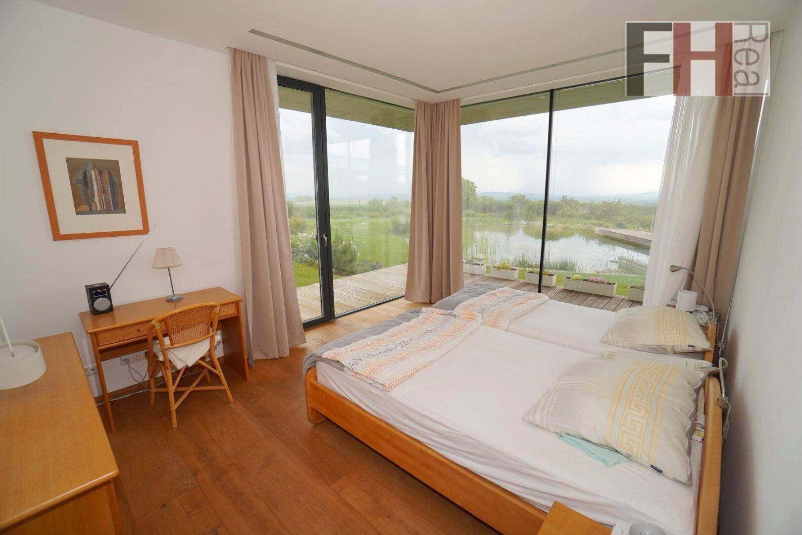 Helles Schlafzimmer mit Holzboden, Schreibtisch und raumhohen Fenstern mit Panoramablick.