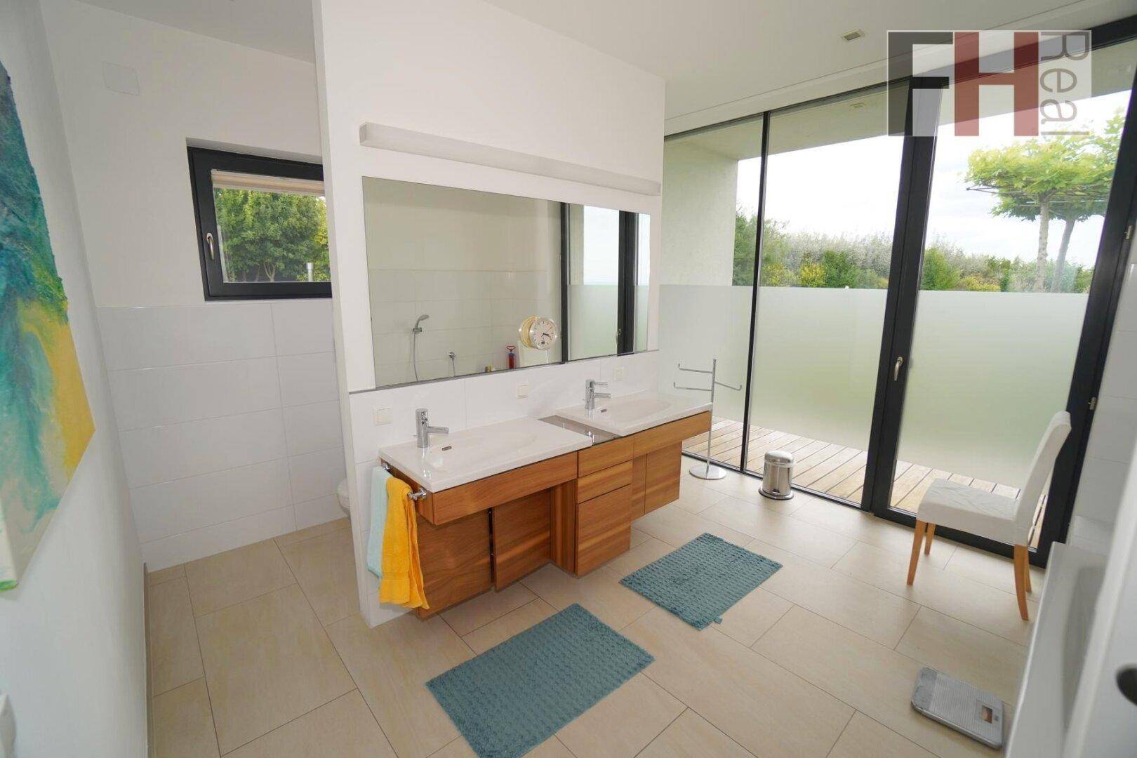 Modernes Badezimmer mit Doppelwaschbecken, großen Fliesen und raumhohen Fenstern.