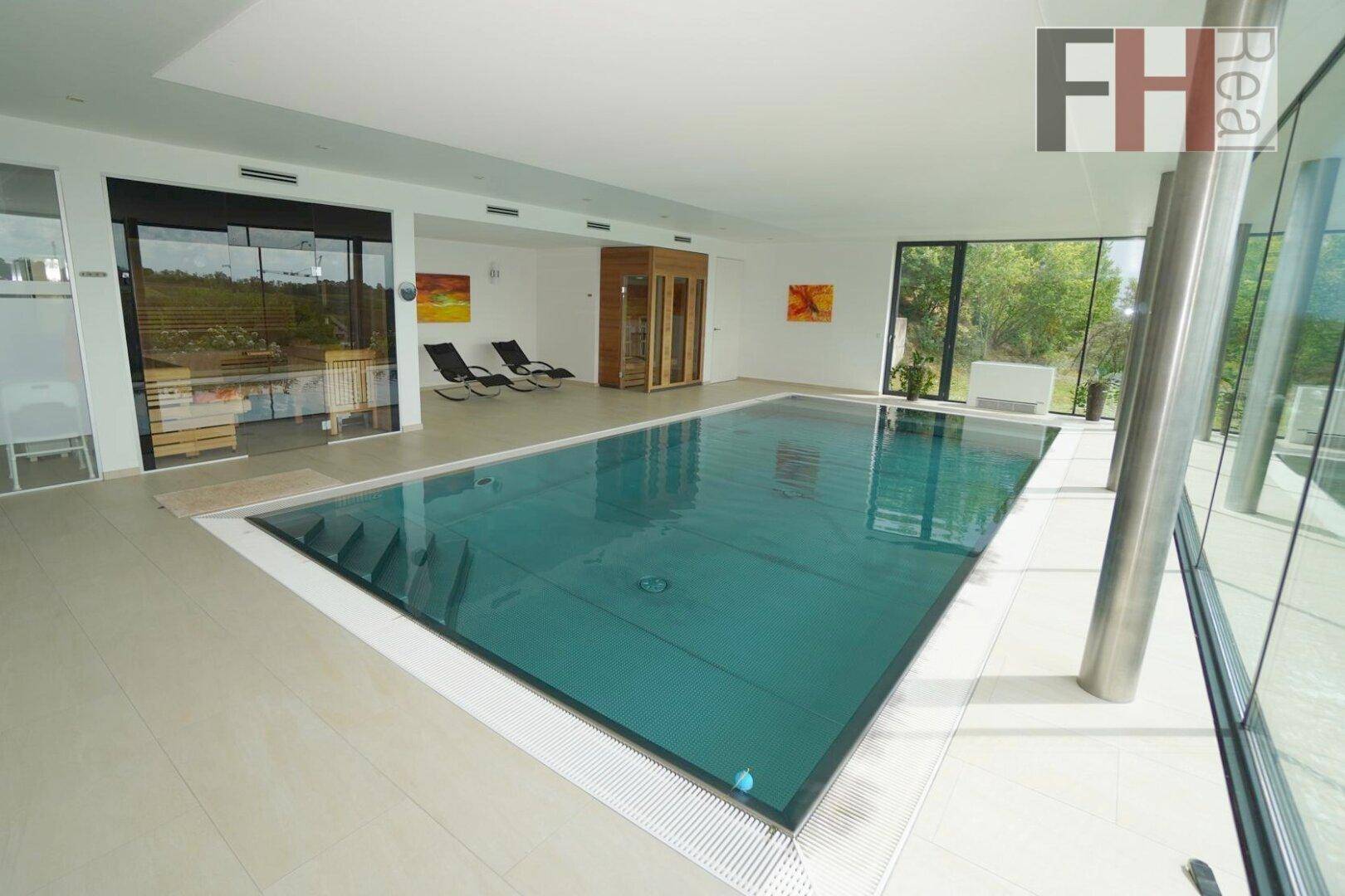 Großer Innenpool mit angrenzendem Wellnessbereich und Panoramablick auf die Landschaft.