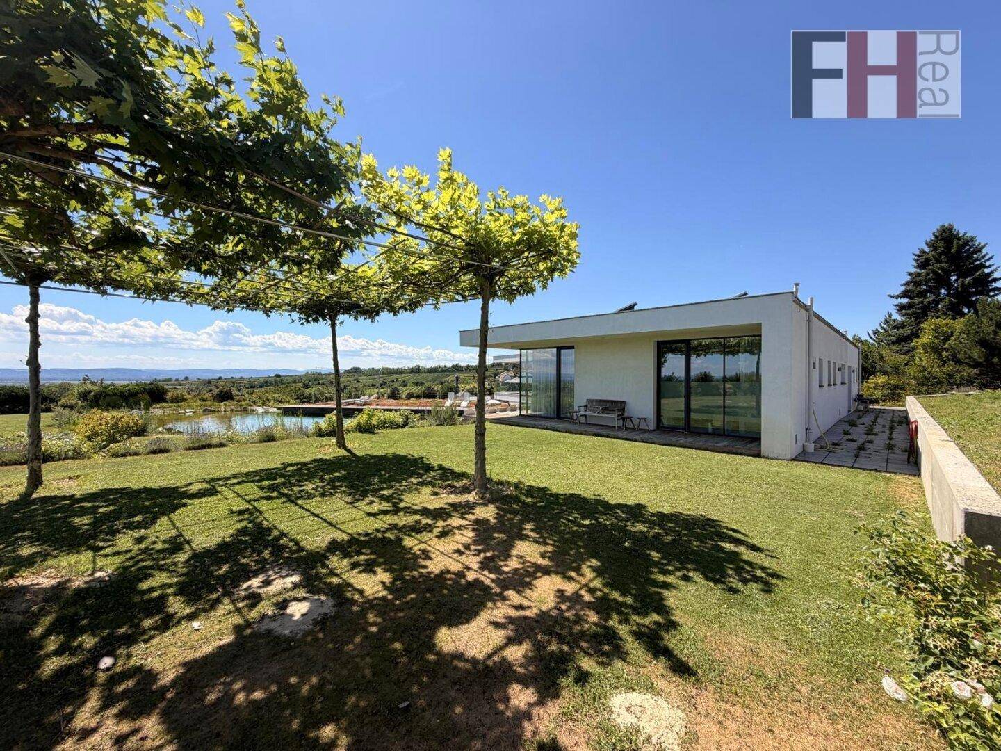 Seitlicher Blick auf die moderne Villa mit Rasenfläche, Bäumen und Fernblick in die Landschaft.