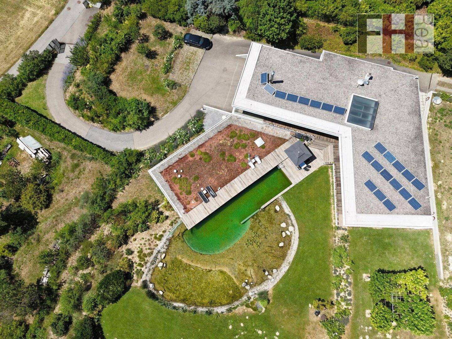 Luftaufnahme der modernen Villa mit Naturschwimmteich, Gründach und Zufahrt.