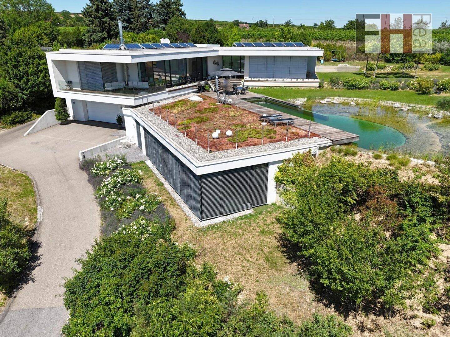 Vogelperspektive der modernen Villa mit Gründach, Naturschwimmteich und weitläufigem Grundstück.