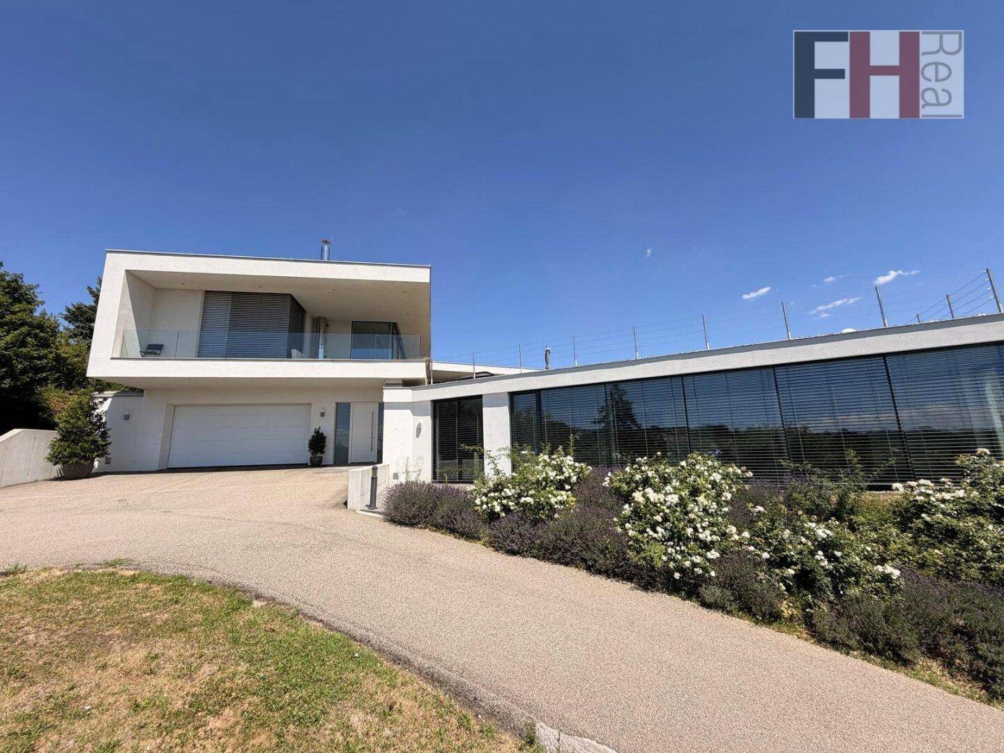 Moderne Architektur der Villa mit großer Garage und weitläufiger Auffahrt unter blauem Himmel.