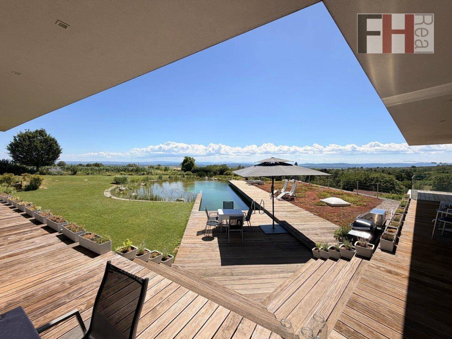 Große Holzterrasse mit Sitzgelegenheiten, Sonnenschirm und weitem Blick über die Landschaft.