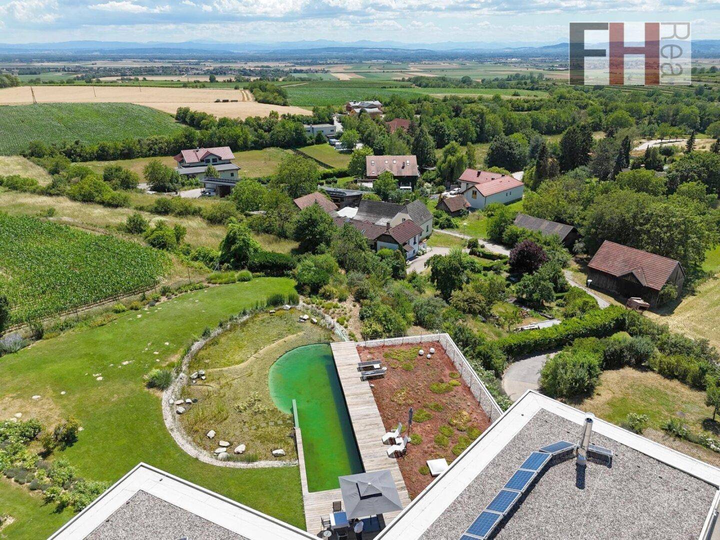 Weitläufige Luftaufnahme der modernen Villa mit Naturschwimmteich und ländlicher Umgebung.