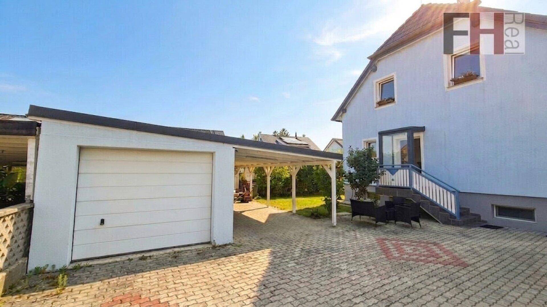 Einfamilienhaus mit Garage, Carport und gepflasterter Einfahrt unter blauem Himmel.