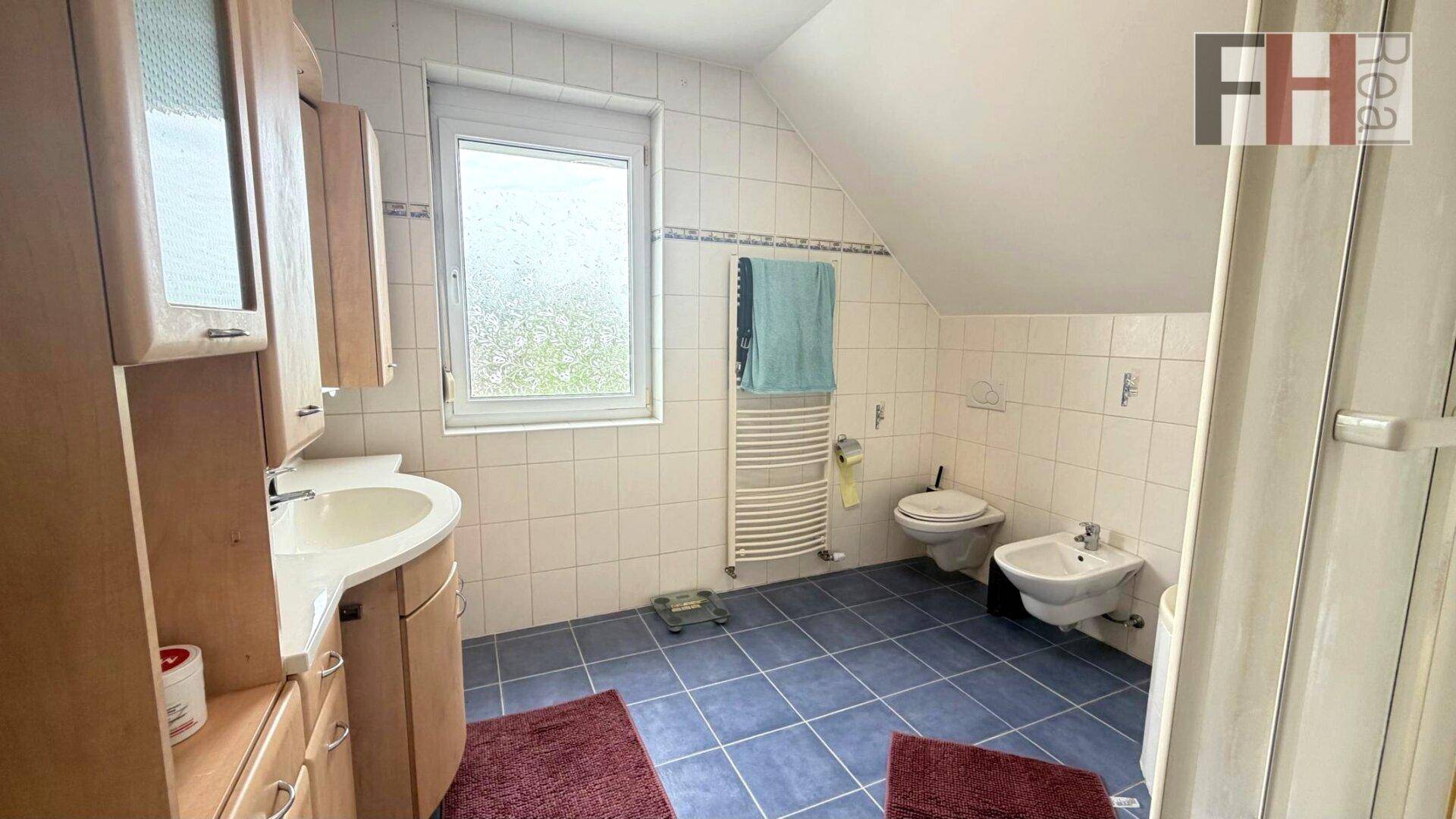 Badezimmer mit Fenster, Bidet, WC und Holzschränken unter der Dachschräge.