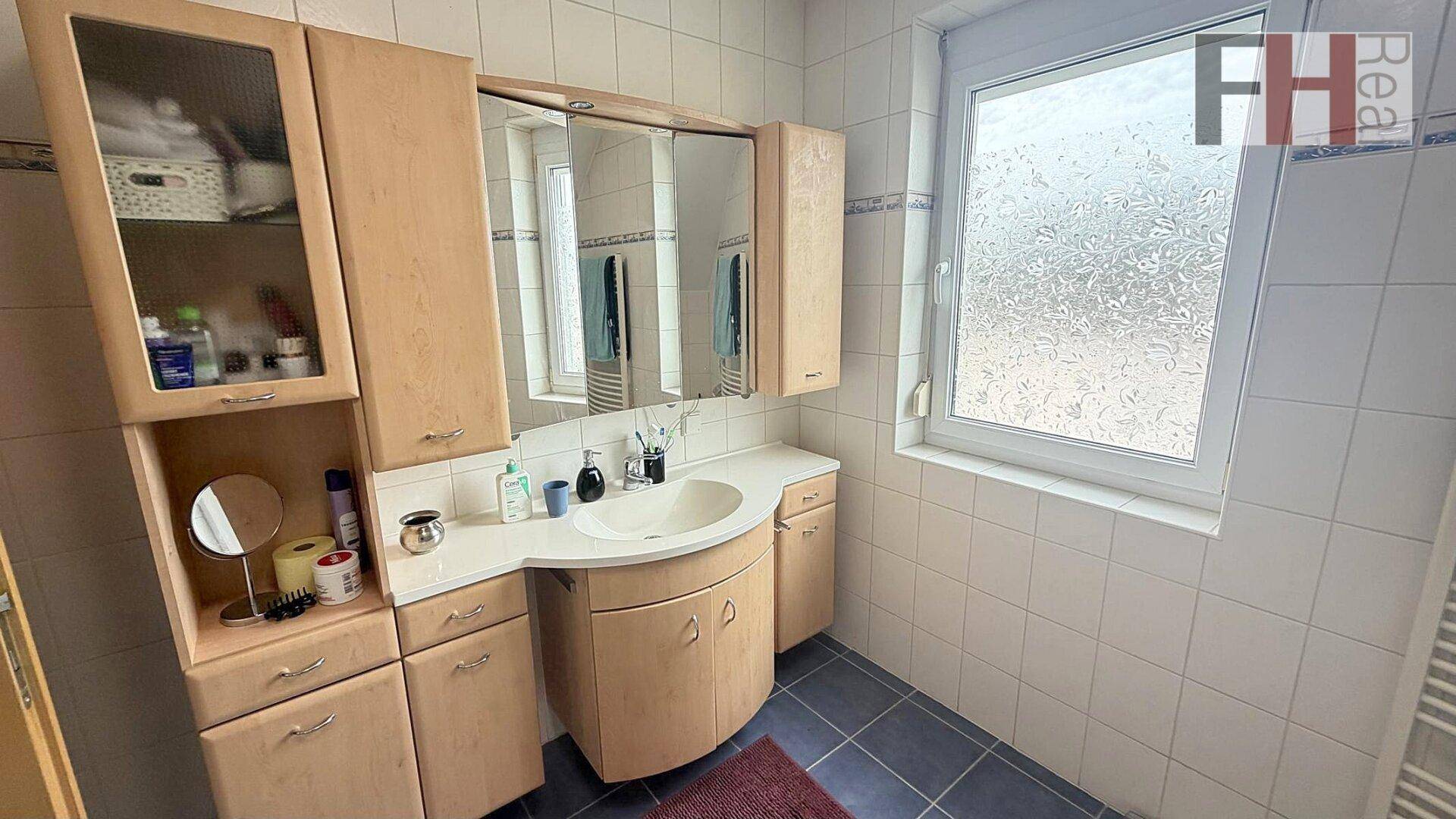Helles Badezimmer mit Holzwaschtisch, Spiegelschrank und Fenster.