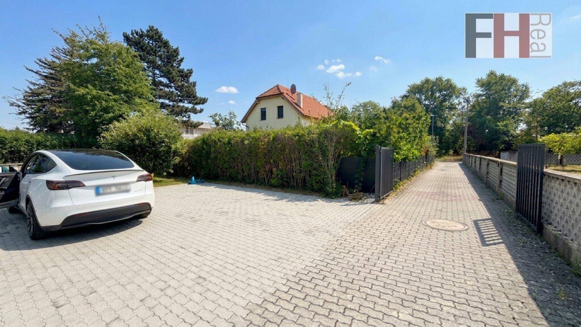 Großer gepflasterter Parkplatz vor dem Haus mit Hecke und Bäumen.