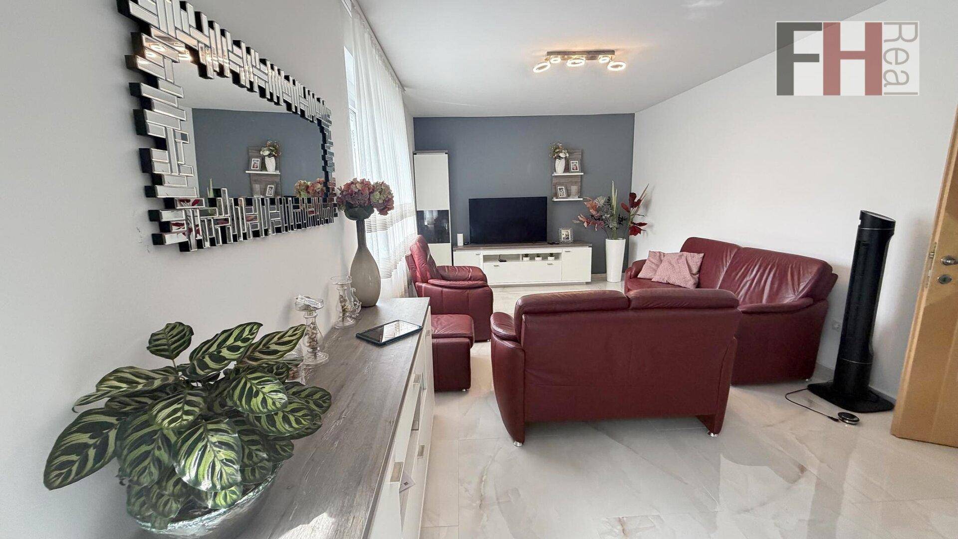Gemütliches Wohnzimmer mit rotem Ledersofa, großem Spiegel und hellem Fliesenboden.