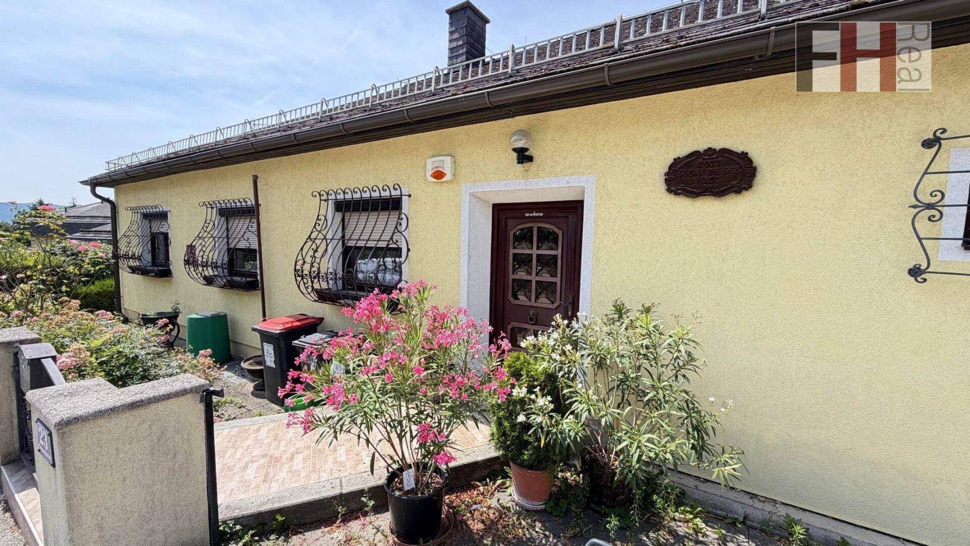 Eingangsbereich des Hauses mit gelber Fassade, Holztür und blühenden Oleanderpflanzen.